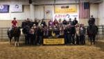 group of equine students in arena with banner, award ribbons & 2 horses